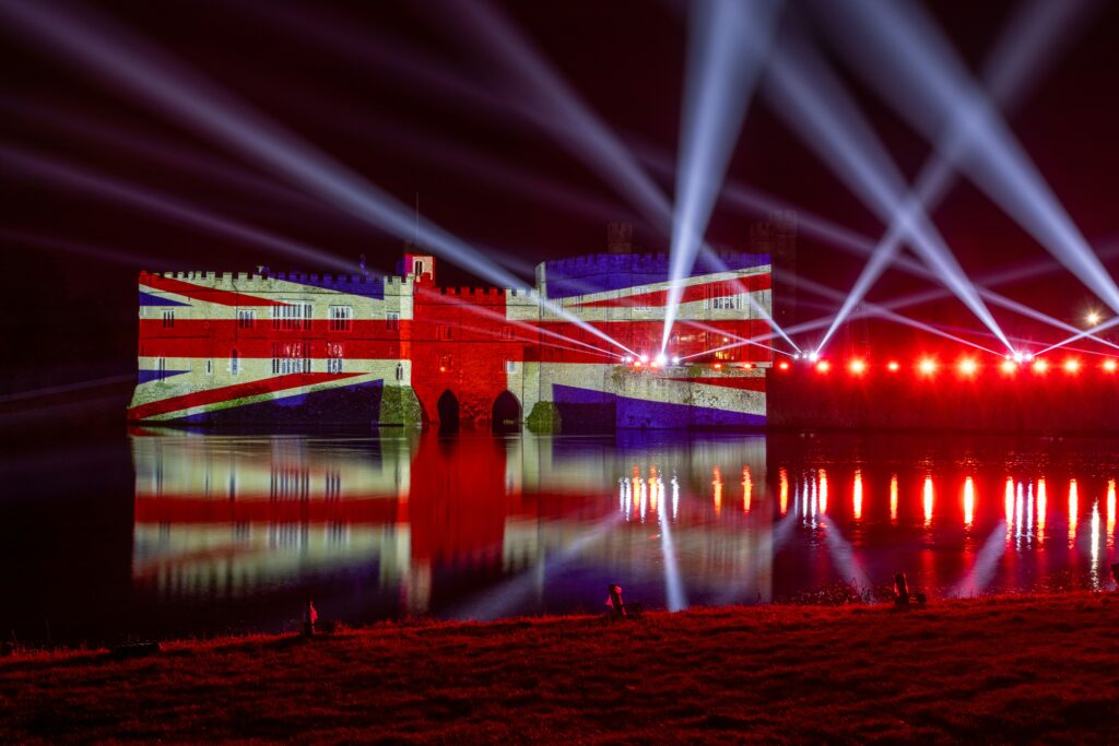 Zamek nad wodą oświetlony na niebiesko, biało i czerwono, w formie flagi Wielkiej Brytanii.