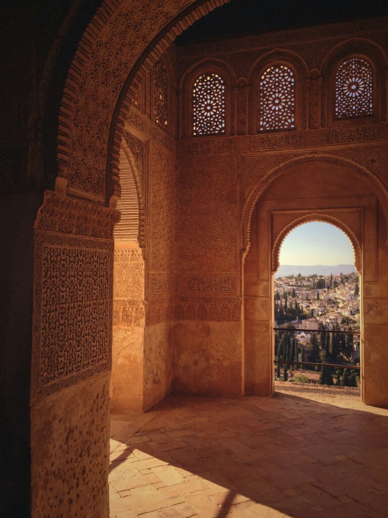 Hiszpańska Alhambra - zacienione pomieszczenie o łukowatych drzwiach i okienkach, kamienie na ścianach rzeźbione w koronkowe wzory.