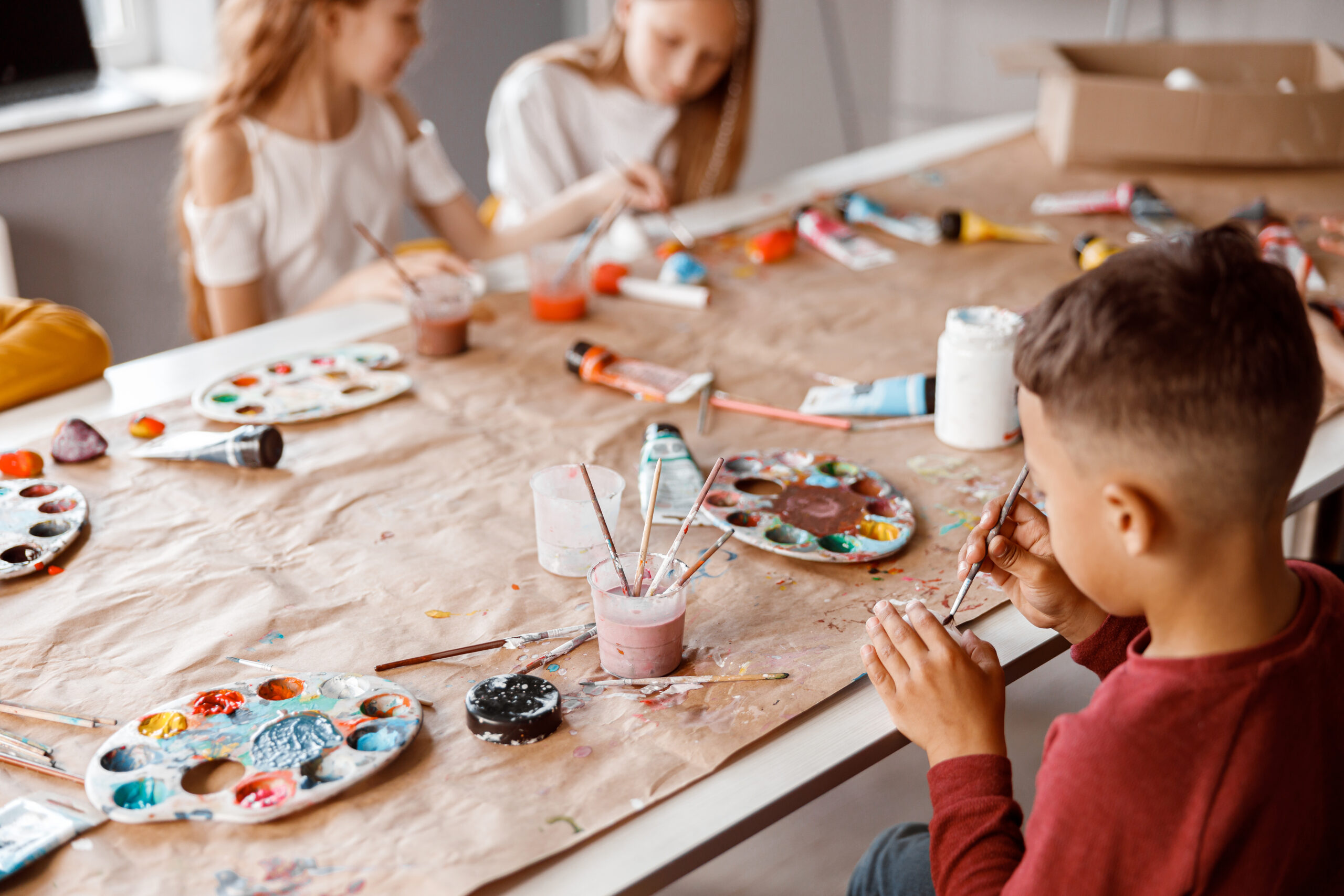 Trójka dzieci maluje farbami na szarym papierze przy długim stole
