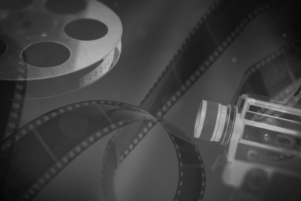Czarno-białe zdjęcie starej kamery i szpuli z taśmą filmową.