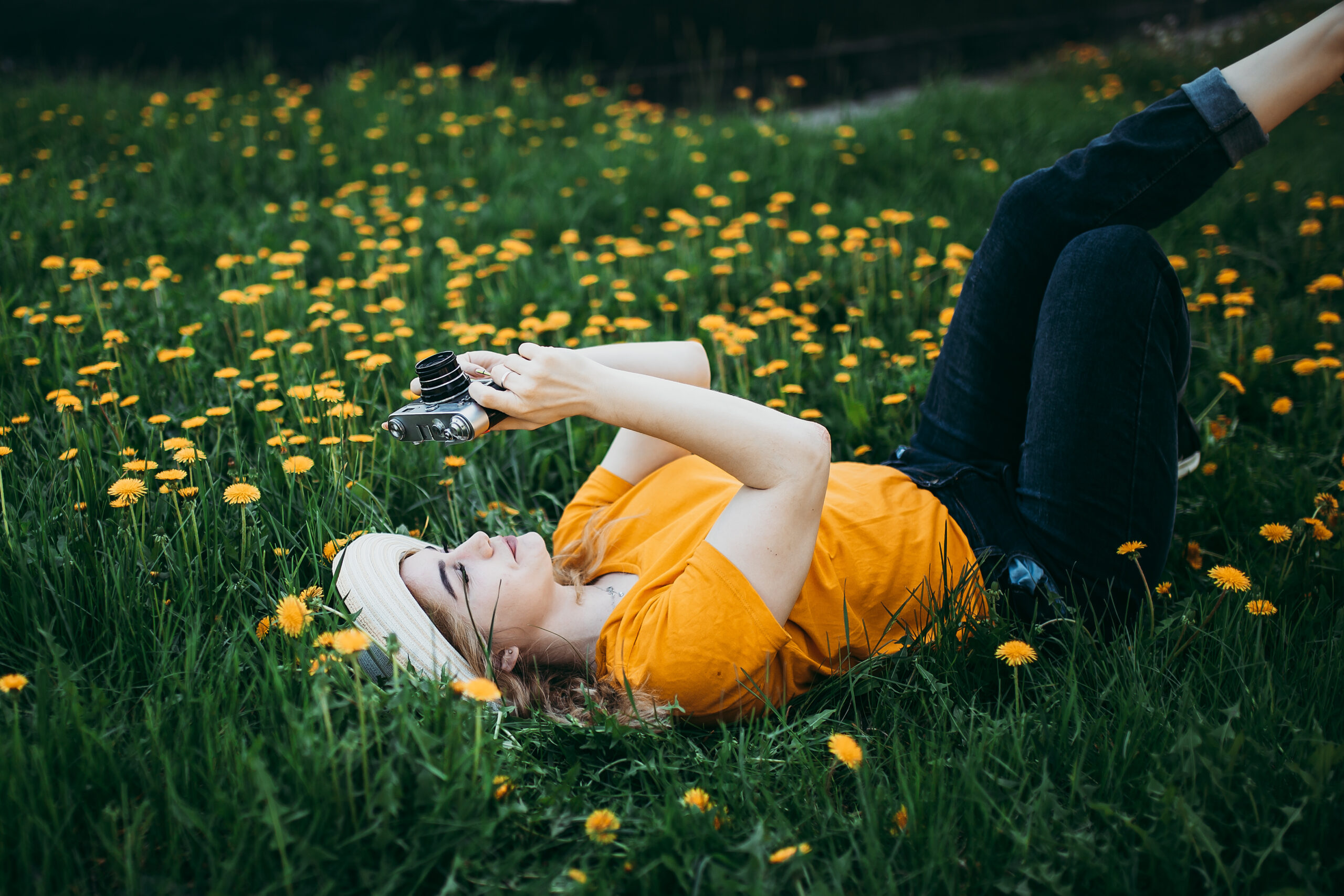 młoda leżąca kobieta w trawie. Trzyma w rękach aparat fotograficzny, skierowany ku niebu