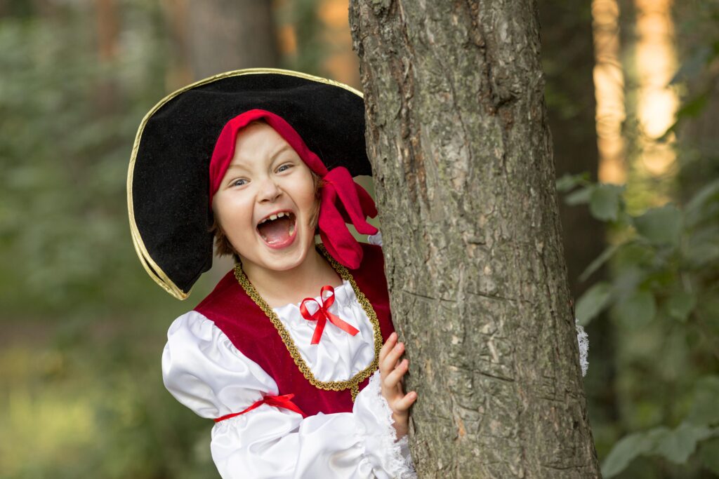 Zdjęcie dziewczynki przebranej za piratkę, która wychyla się zza drzewa.