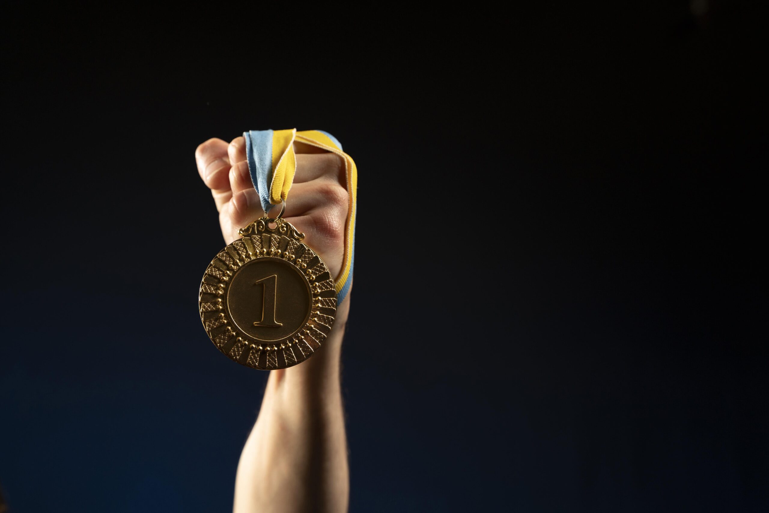 Na zdjęciu widać rękę trzymającą duży złoty medal z numerem jeden