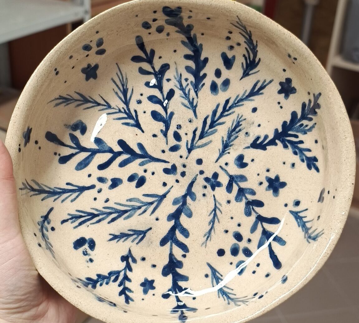 Zbliżenie na ręcznie robiony ceramiczny talerzyk. Talerz jest jasny, ozdobiony drobnymi niebieskimi wzorami liści i kwiatów.