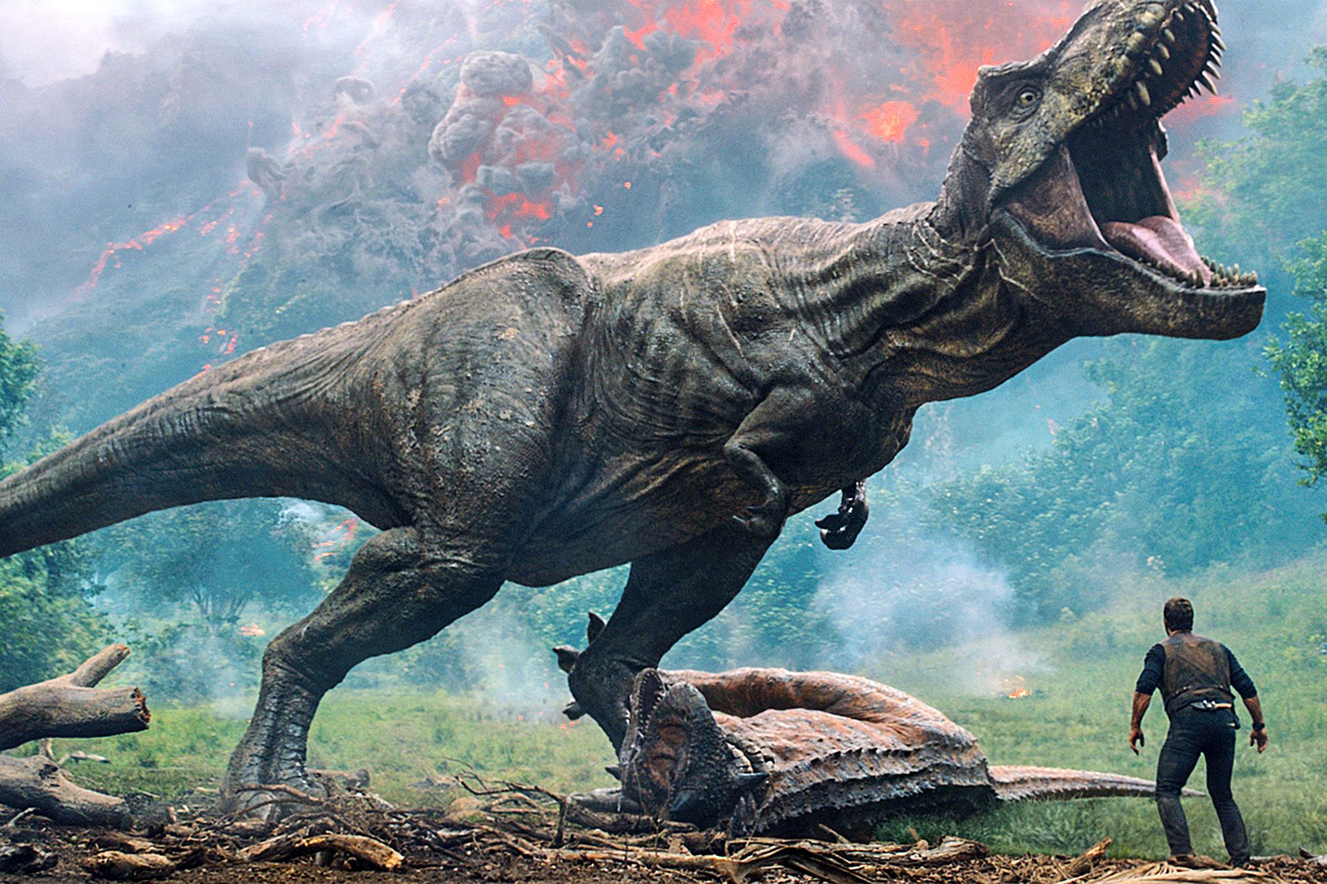 Kadr z filmu Jurrasic World: wielki tyranozaur z otwartą paszczą szarżuje na człowieka w prawym dolnym rogu obrazu. U stóp dinozaura ciało innego gada.