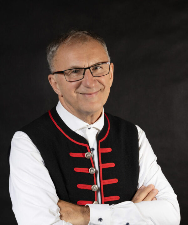 Zdjęcie portretowe Grzegorza Poloczka. Mężczyzna w okularach ubrany w białą koszulę oraz czarną kamizelkę.